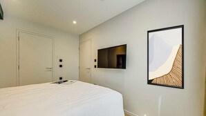 Ett modernt hotellrum med en stor säng, en platt-TV som är monterad på väggen och ett inramat, abstrakt konstverk.