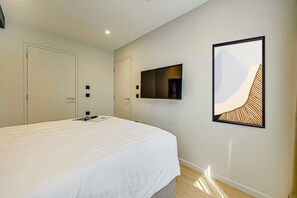 Ein modernes Hotelzimmer mit einem großen Bett, einem flachbildfernseher an der Wand und einem gerahmten abstrakten Kunstwerk.