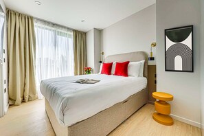 Ein modernes Hotelzimmer mit einem großen Bett, einem Nachttisch und einem an der Wand befestigten Kunstwerk.