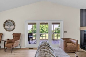 Ein Wohnzimmer mit einer großen Glasschiebetür, die auf eine Terrasse im Freien führt, zwei Ledersessel, ein Sofa und ein Kamin.