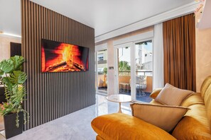 En moderne stue med et fladskærms-TV, en sofa, et rundt bord og en potteplante.