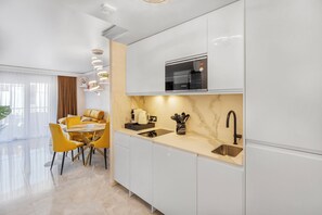 Eine moderne Küche mit weißen Schränken, einer eingebauten Mikrowelle und einem Spülbecken. Es gibt einen Essbereich mit gelben Stühlen und einem Tisch.