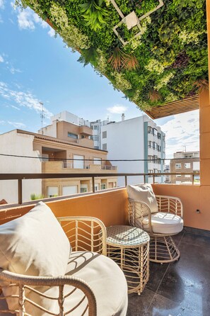 Ein Balkon mit Korbmöbeln, einer grünen Wand und Blick auf Gebäude.