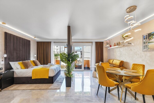 Habitación de hotel moderna con cama, una mesa de comedor con sillas, una planta en maceta y vistas a través de una puerta de cristal.