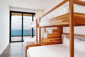 Ein Hotelzimmer mit einem Holzbettgestell, einem Einzelbett, einem großen Fenster mit Meerblick und einer Schiebeglastür.
