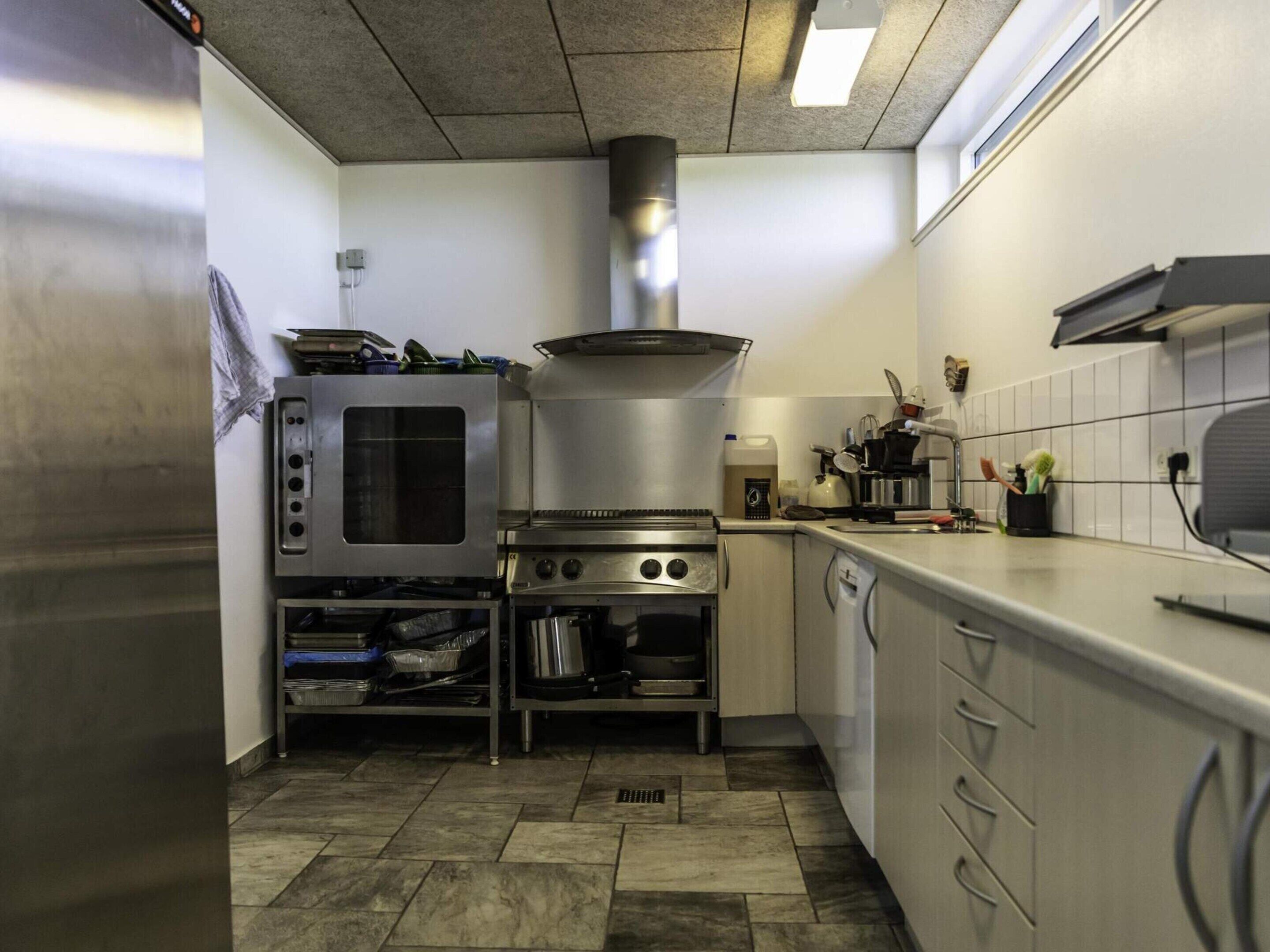 A kitchen with stainless steel appliances, a microwave, oven, and a range hood. There is a dish rack, a coffee maker, and a sink.