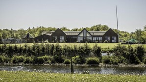 Un bâtiment moderne doté d’une grande façade en verre, entouré d’une zone verdoyante et bordé par un plan d’eau.