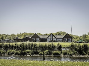 A modern building with a large glass facade, surrounded by a grassy area and a body of water. - 4 Star Holiday Home in Aabybro (Aabybro)