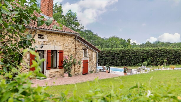 Une maison en pierre avec des volets rouges, une piscine et un jardin.