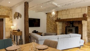 Un salon chaleureux avec une cheminée en pierre, un canapé et une table à manger préparée pour deux personnes.