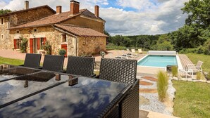 Une maison en pierre avec une piscine, du mobilier d’extérieur et un ciel dégagé.