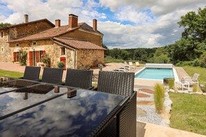 Ein Steinhaus mit Swimmingpool, Gartenmöbeln und blauem Himmel.