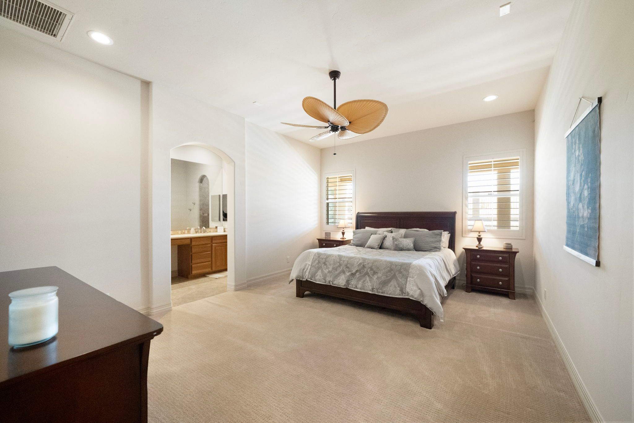 A bedroom with a bed, nightstands, a ceiling fan, and a bathroom with a vanity.