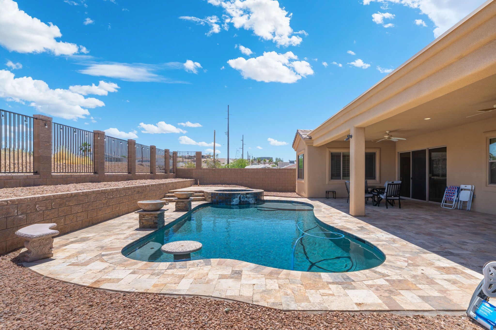 Una piscina con hidromasaje, baldosas de piedra y un área de patio cubierta.
