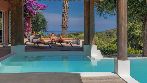 A pool area with two lounge chairs and a person reading a book. - La Ty Kaz – Cocon entre mer, maquis et piscine en Costa Verde (Valle-di-Campoloro)