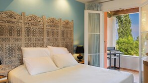 A bedroom with a large bed, a decorative headboard, a nightstand, a lamp, and a view of the outdoors. - La Ty Kaz – Cocon entre mer, maquis et piscine en Costa Verde (Valle-di-Campoloro)
