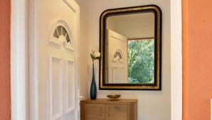 A hallway with a white door, a mirror with a gold frame, a wooden cabinet, and a vase with flowers. - La Ty Kaz – Cocon entre mer, maquis et piscine en Costa Verde (Valle-di-Campoloro)