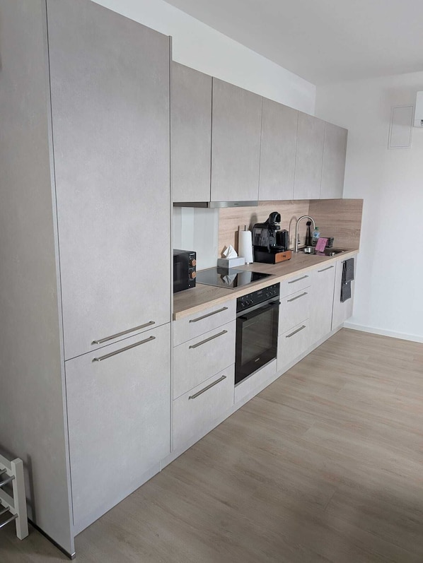 A modern kitchen with grey cabinets, a built-in oven, and a coffee machine.