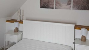 A bedroom with a sloped ceiling, a bed, two bedside tables with lamps, and two wall-mounted pictures. - Small cozy vacation apartment on the 1OG (Werther (Westfalen))