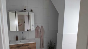 A modern bathroom with a white vanity, a mirror, a towel rack, and a potted plant. - Small cozy vacation apartment on the 1OG (Werther (Westfalen))