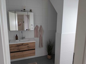 Une salle de bain moderne avec un meuble-lavabo blanc, un miroir, un porte-serviettes et une plante en pot.
