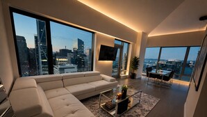 Ein modernes Wohnzimmer mit einer großen Couch, einem Glastisch und Blick auf die Stadt durch große Fenster.