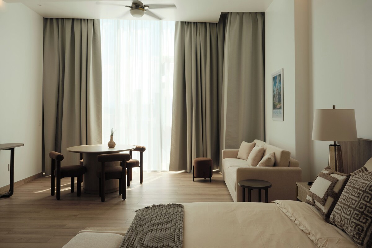 Ein Hotelzimmer mit Bett, Sofa, Esstisch mit Stühlen, Deckenventilator und Lampe.