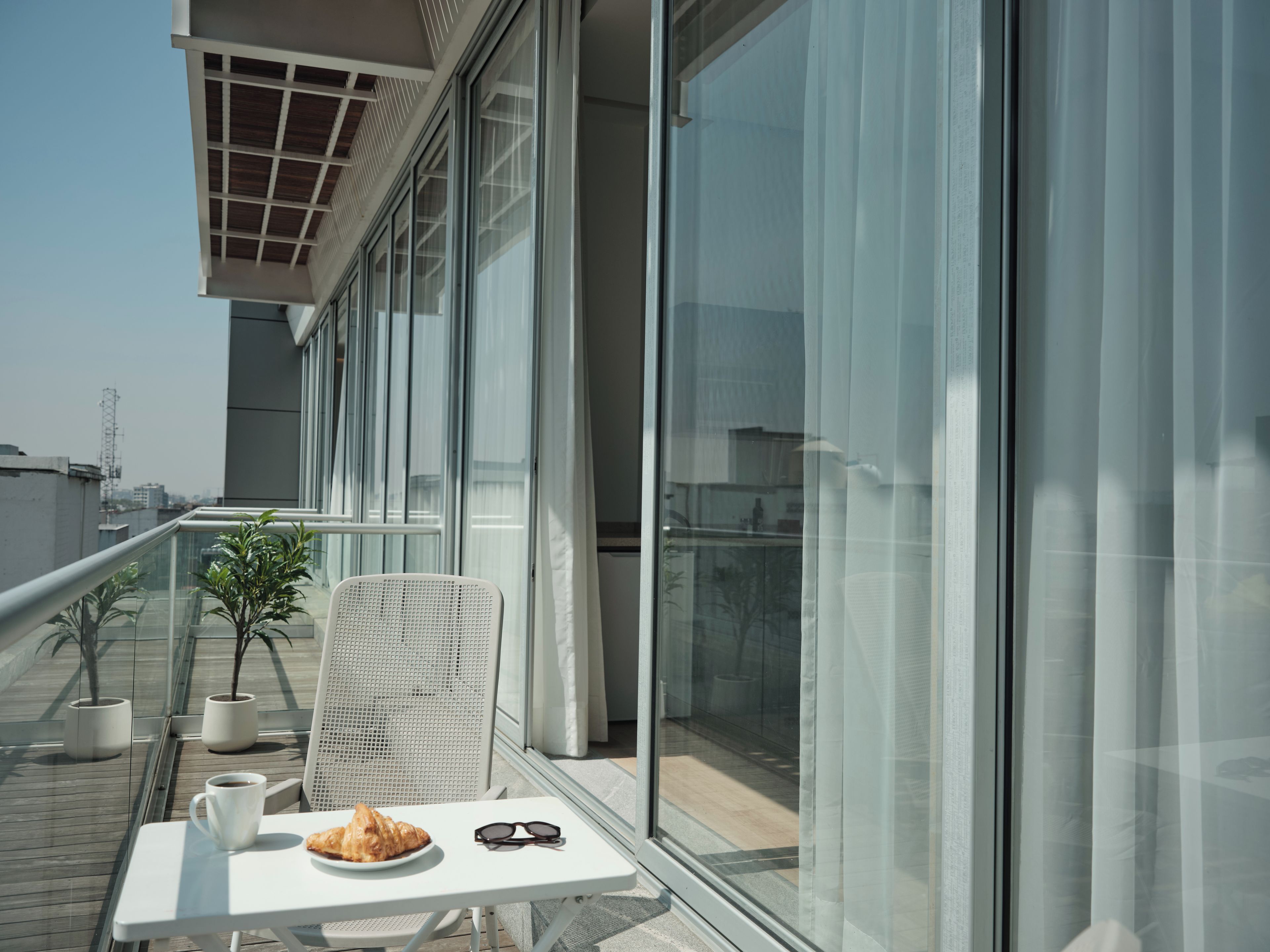 Uma varanda com mesa, cadeira, um prato de comida, xícara e um par de óculos de sol.