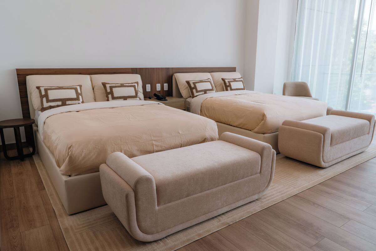 A modern hotel room with a large bed, a smaller bed, a sofa, and a chair.