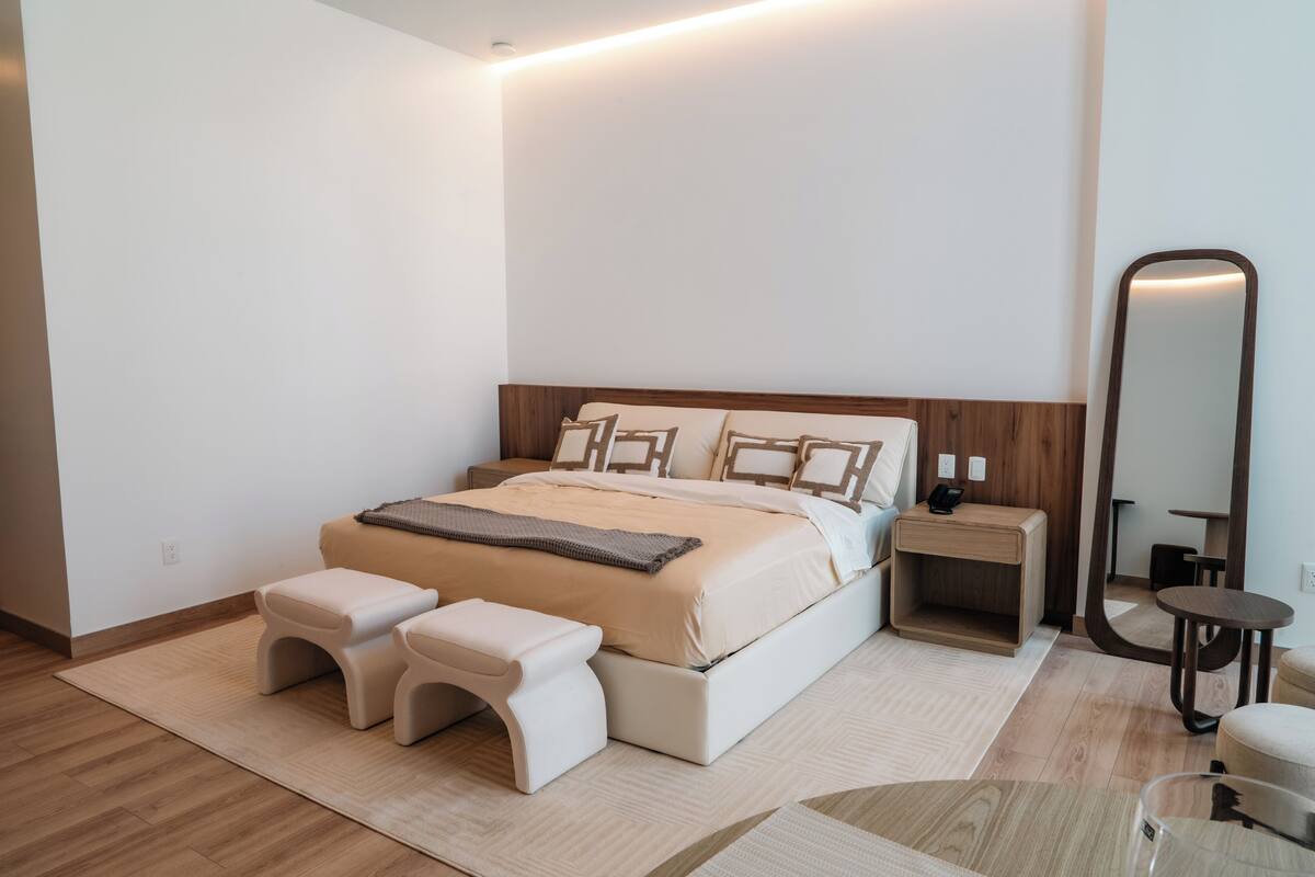 A bedroom with a bed, two bedside tables, a nightstand, a mirror, and a small round table.