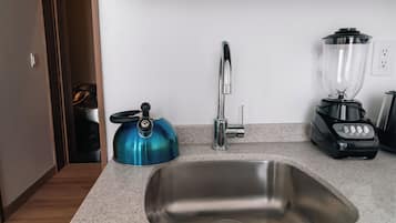 A kitchen with a stainless steel sink, a blue kettle, a blender, and a faucet.
