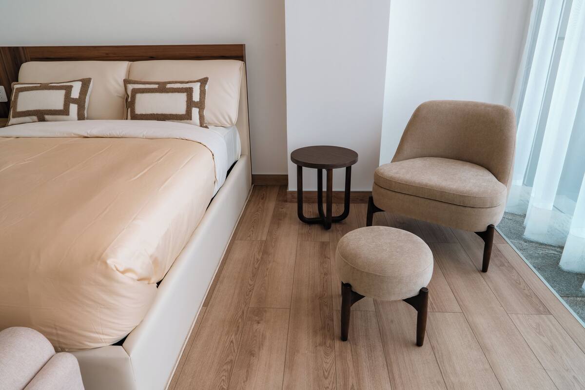 A hotel room with a bed, a round table, a chair, and a small ottoman.