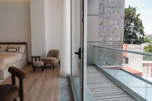 A hotel room with a bed, two armchairs, a small table, and a balcony with a view of the outside. - Roma Residence Luxury Suites  (Ciudad de México)