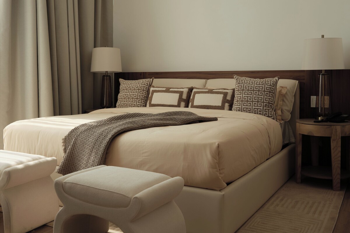 Ein modernes Schlafzimmer mit einem großen Bett, Nachttischen, einer Bank und einem Teppich.