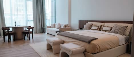 A modern bedroom with a large bed, bedside tables, a sofa, and a dining area with chairs.