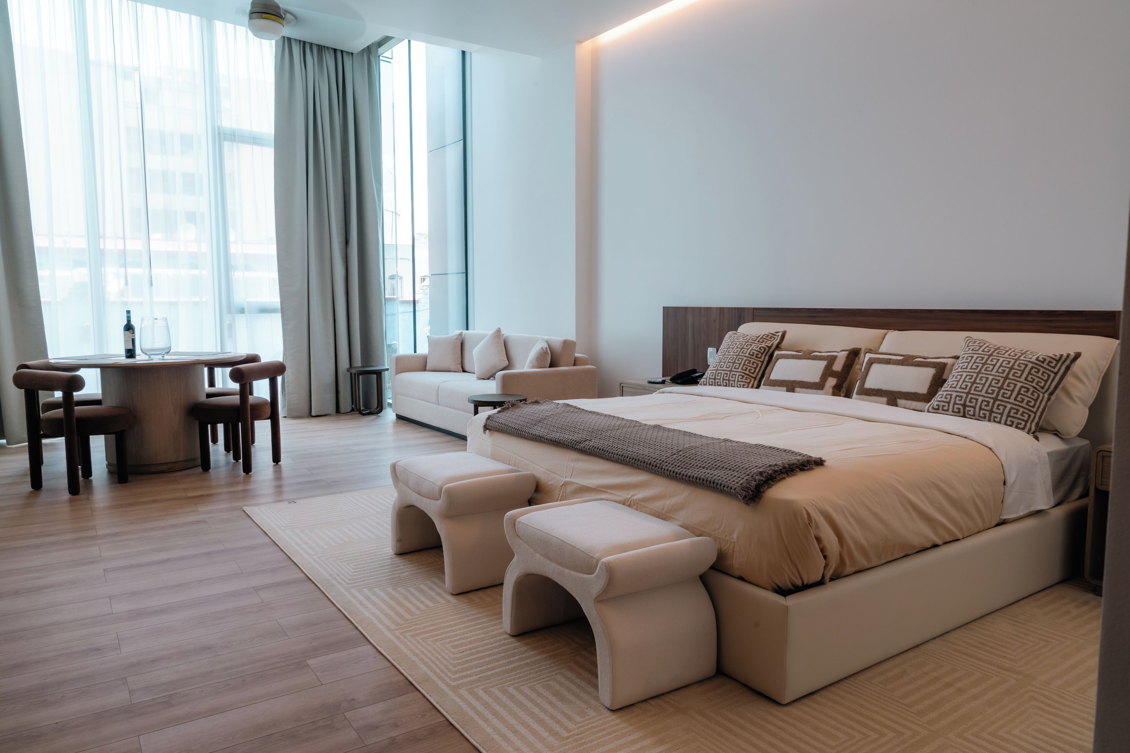A modern bedroom with a large bed, bedside tables, a sofa, and a dining area with chairs.