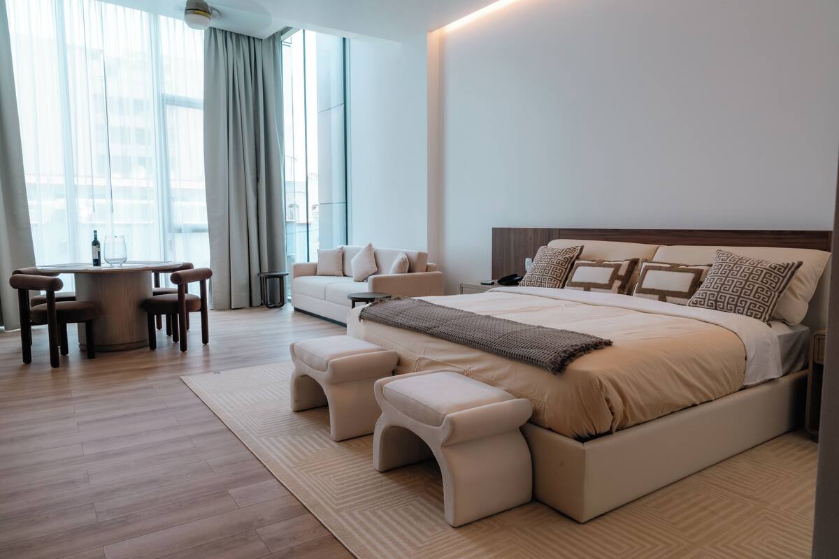 A modern bedroom with a large bed, bedside tables, a sofa, and a dining area with chairs.