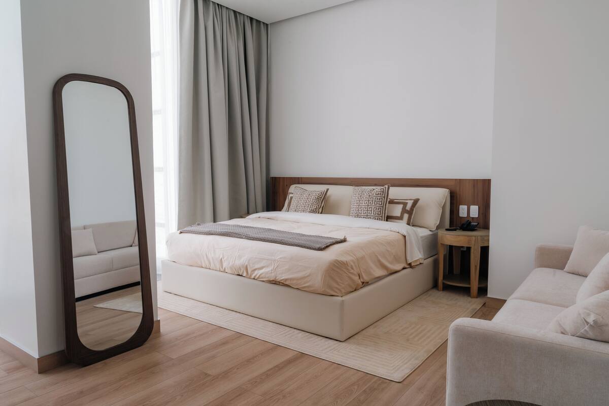 A modern bedroom with a large bed, a bedside table, a chair, and a mirror.