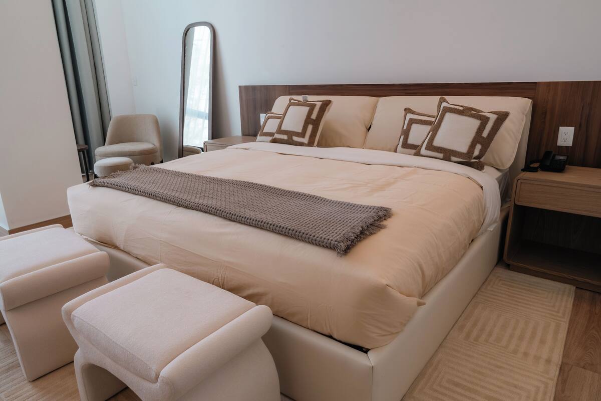 A bedroom with a large bed, two bedside tables, a chair, and a mirror.