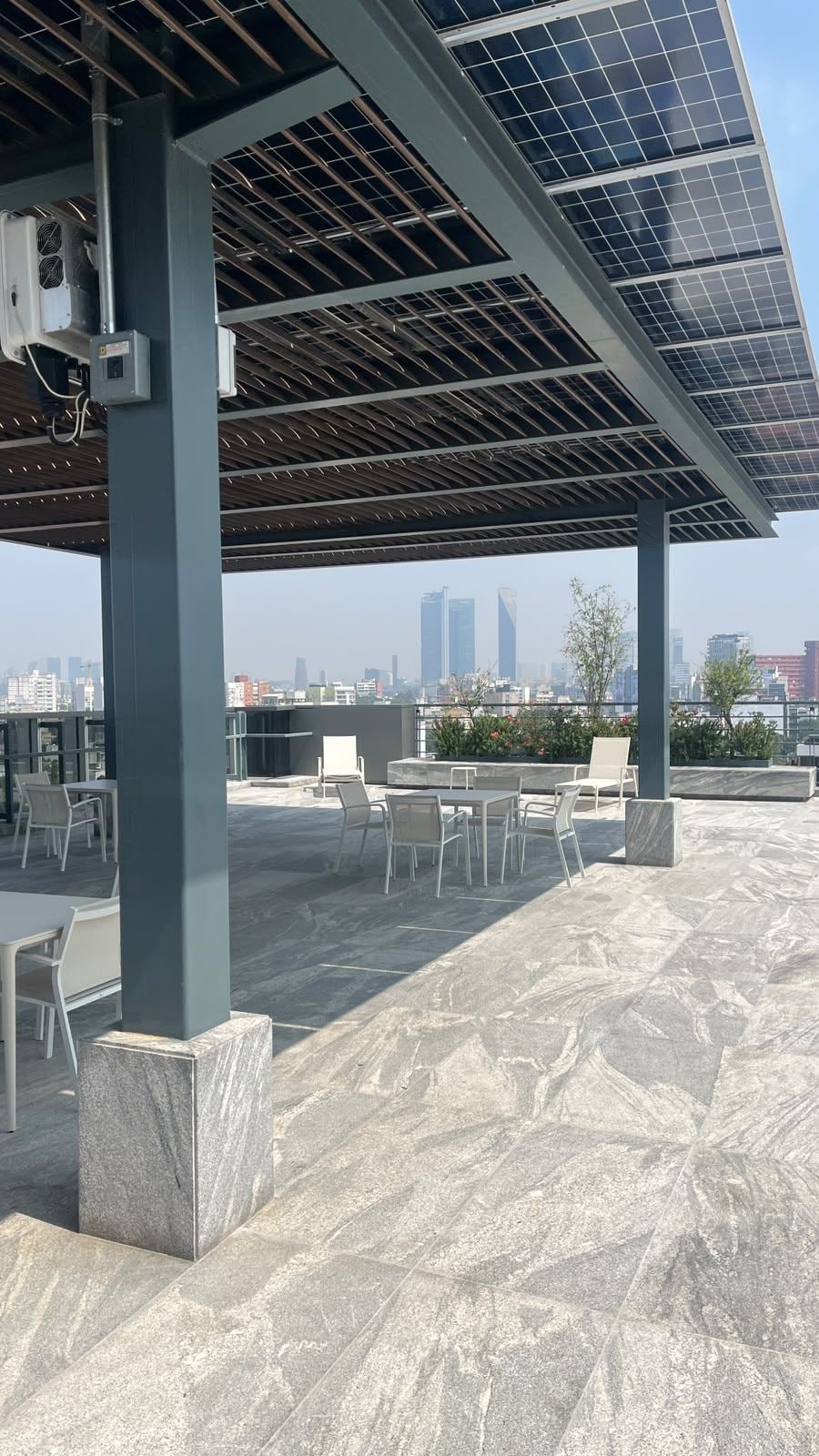 Un espace extérieur aménagé avec des sièges, doté d’un toit recouvert de panneaux solaires, avec une vue sur les gratte-ciel de la ville en arrière-plan et un ciel dégagé.