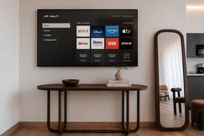 A modern living room with a mounted TV displaying a streaming service interface, a round table with a bowl and books, and a large mirror. - Roma Residence Luxury Suites  (Ciudad de México)