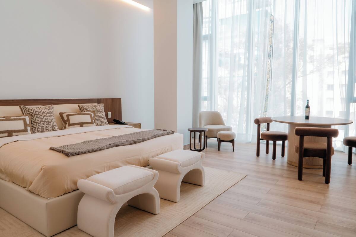 A modern bedroom with a large bed, bedside tables, a round dining table, and chairs.