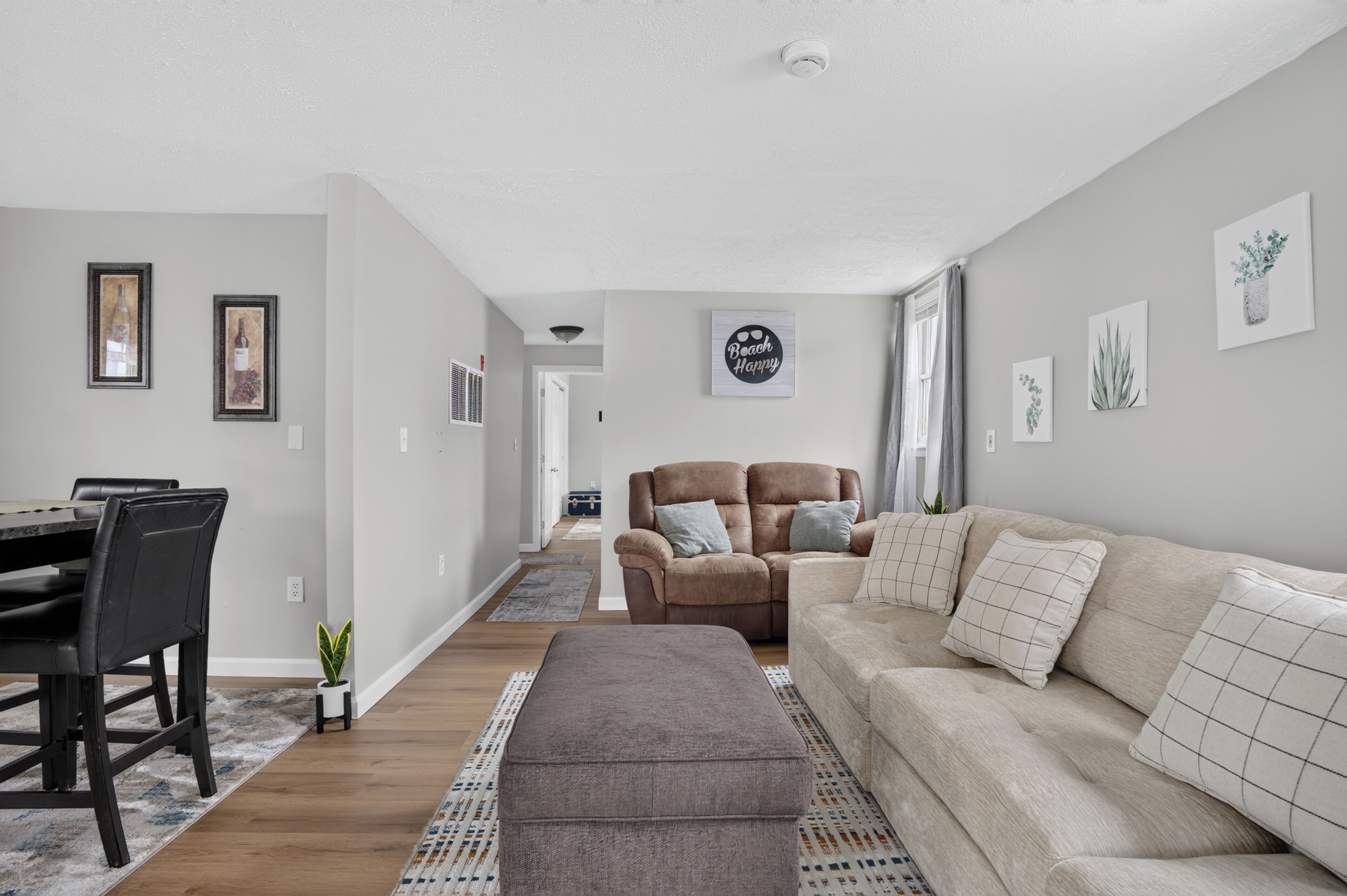 Ein modernes Wohnzimmer mit Essbereich, einem braunen Ledersofa, einem beige farbenen Sofa und einem grauen Hocker.