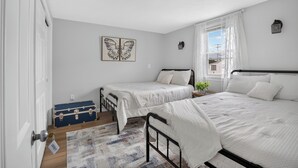 Un dormitorio con dos camas, una ventana con cortinas, una lámpara fijada a la pared y un cuadro decorativo de una mariposa.