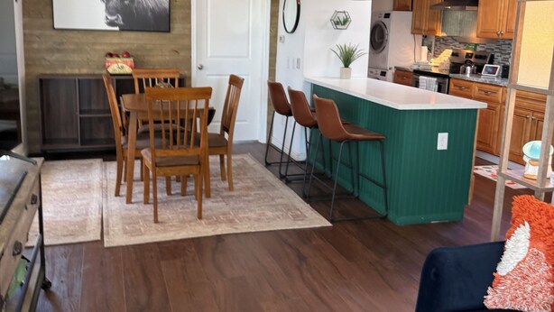 A modern kitchen with wooden cabinets, a central island, and a dining area with a table and chairs. - Charming 2 BR Little Oasis, with  pool, near Colorado River, SNOWBIRD FRIENLDY (Bullhead City)