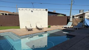 A rectangular swimming pool with a tiled edge, surrounded by a patio area with lounge chairs and a wooden fence. - Charming 2 BR Little Oasis, with  pool, near Colorado River, SNOWBIRD FRIENLDY (Bullhead City)