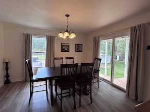 A dining area with a table and chairs, a chandelier, and large windows with curtains.