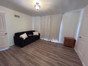 A room with a black sofa, a wooden dresser, white curtains, and a ceiling light fixture.