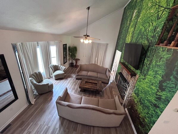 A living room with a sofa, armchairs, a coffee table, a fireplace, and a large green wall mural.
