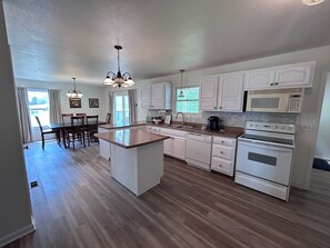 A kitchen with white cabinets, a central island, a dining area with chairs, and a view through the window.